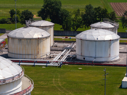 Aerial view of several oil storage tanks located at a petroleum facility during daylight. Tanks are arranged in a large industrial area.