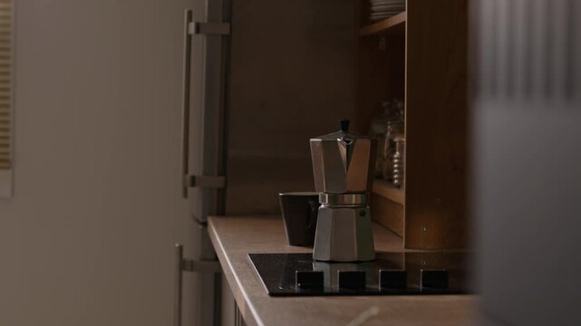 Moka pot standing on induction stove next to coffee cup during morning routine. Footage suitable for food and beverage advertising or morning lifestyle campaigns