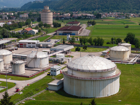 Drone view shows an oil storage facility with large tanks and industrial structures near a town and fields.