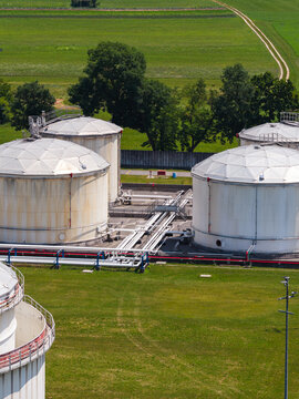 Drone view shows multiple oil storage tanks at a fuel terminal in a rural area surrounded by green fields.