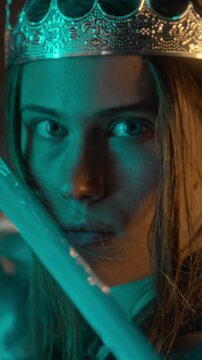 Portrait of Caucasian young woman wearing crown raising sword blade in front of face, vertical. Footage ideal for fantasy film trailer, medieval cinema teaser, and roleplay gaming campaign