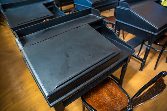 Vintage wooden school desks arranged in classroom setting with wooden flooring and natural light streaming through the windows in Halki Theological School