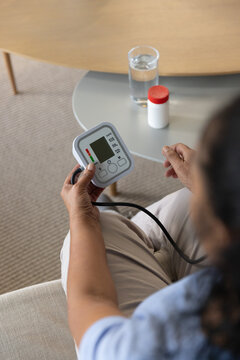 Senior African American woman wearing blue top checking BP monitor on sofa, copy space