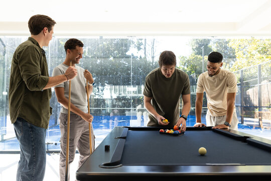 Male friends gathering around black-felt pool table in game room, arranging racked billiard balls