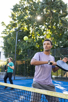 Two male players volleying at net on blue court with purple shirt, paddle and yellow ball