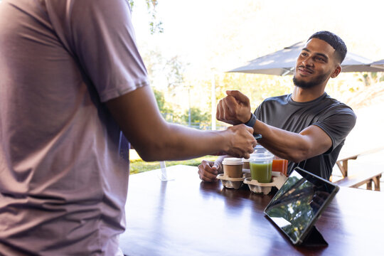 African American men exchanging drinks at wooden patio counter with drink carrier and tablet
