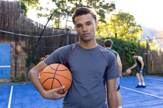 Three males standing on blue court holding orange basketball wearing athletic shirts dribbling
