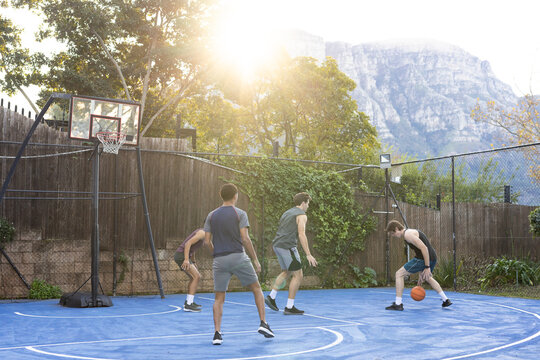 Male friends playing pickup basketball on blue court, in shorts, dribbling orange ball, copy space