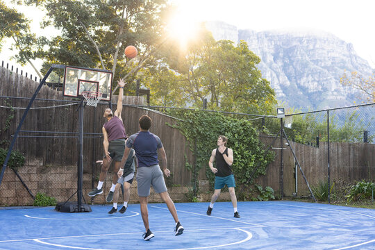 Diverse male friends playing basketball on blue court, purple-shirt jumper reaching for basketball