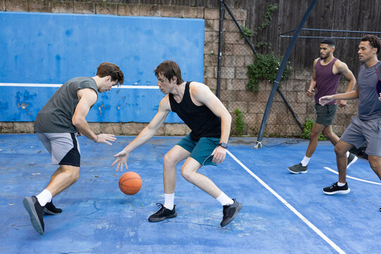 Male friends playing pickup basketball on blue court, dribbling, defending, moving toward hoop