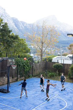 Diverse male friends playing pickup basketball on blue court, shooting orange ball toward hoop
