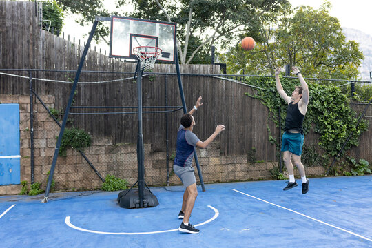 Diverse male friends playing on blue half-court with portable hoop and orange ball, copy space