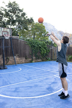 Adult male shooting basketball on blue yard court with portable hoop wearing tank top, copy space