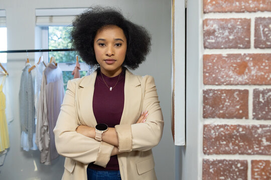 African American woman standing with arms crossed in boutique fitting room by clothing rack