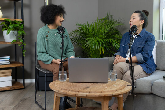 Diverse female co-hosts recording podcast in home studio with microphones, laptop and green sweater