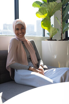 African American woman sitting on sofa in office lounge wearing pink hijab, fiddle leaf fig