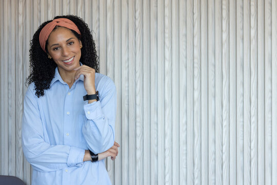 African American woman posing with coral headband, touching chin by white slat wall, copy space