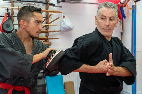 Hapkido student practicing an arm block technique with an instructor holding a focus mitt in a martial arts dojo