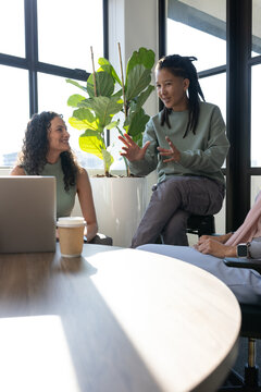 Diverse coworkers listening, speaker gesturing on stool by office table with open laptop