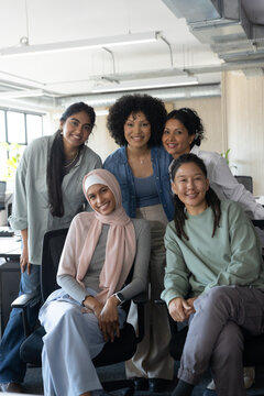 Diverse coworkers posing together in modern open-plan office with monitors, plants, wooden wall