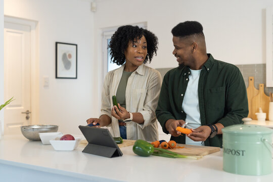 Couple chopping vegetables and following tablet recipe at home kitchen island with compost canister