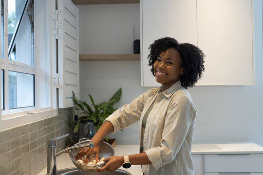 Woman rinsing pale round food items in metal colander at kitchen sink under faucet, copy space