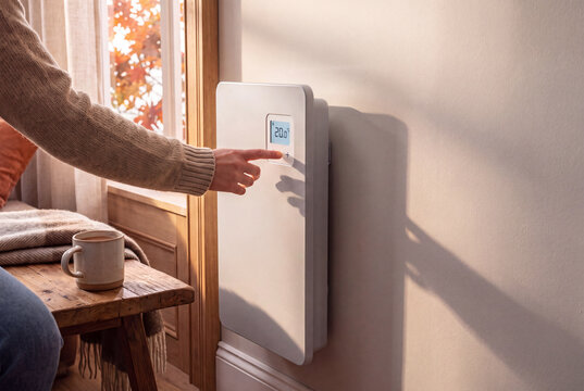 Personne r&eacute;glant un radiateur &eacute;lectrique moderne avec thermostat num&eacute;rique dans un int&eacute;rieur chaleureux en automne, concept de confort thermique et d&rsquo;&eacute;conomie d&rsquo;&eacute;nergie