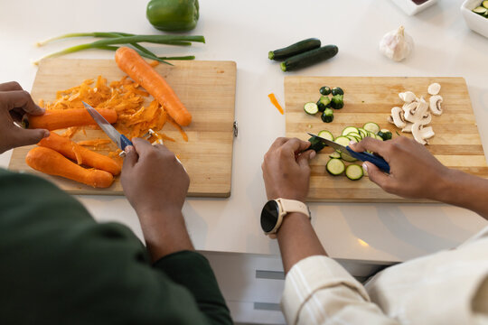 African American couple peeling carrots slicing zucchini on white countertop with cutting boards