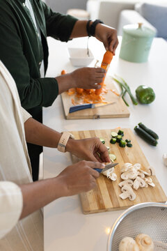 African American couple chopping mushrooms, peeling carrot on white kitchen countertop with peeler