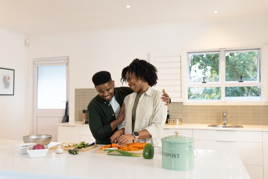 African American couple preparing meal in home kitchen using cutting board and compost can