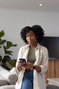 Woman standing in living room holding smartphone and smiling while wearing smartwatch