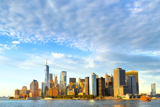 View of the Lower Manhattan skyline featuring One World Trade Center and various skyscrapers along the waterfront under a blue sky with scattered clouds, New York, New York, United States.