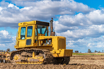 Agricultural view of yellow bulldozer cultivating soil with disc harrow under cloudy blue sky. © Todayphoto