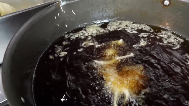 Crispy seafood pieces fry inside a large metal pan filled with boiling oil, then drain on absorbent paper towels in a restaurant kitchen environment