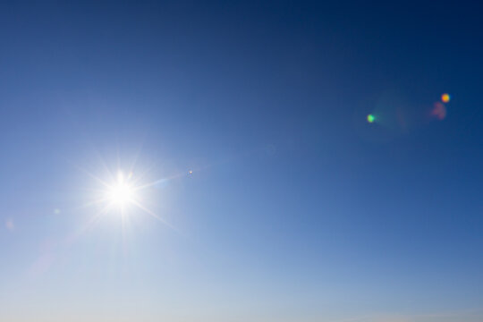 Bright midday sun shines in a clear blue sky, sending radiant sunlight rays and subtle lens flare to create a warm, airy, optimistic atmosphere suitable for backgrounds, weather and nature concepts