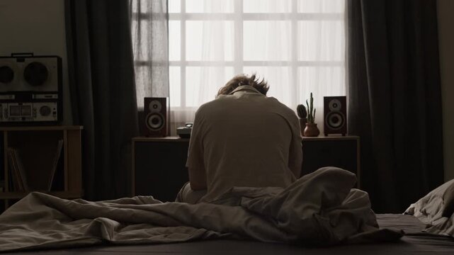 Caucasian young adult man waking up, sitting on bed, and standing up to start day, rear view. Perfect for sleep disorder awareness, morning routine commercials, and mental health videos
