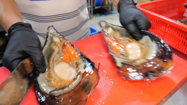 Professional culinary preparation of fresh giant sea clams involving shell opening, internal meat separation, and precise trimming on a red cutting board for commercial seafood dining