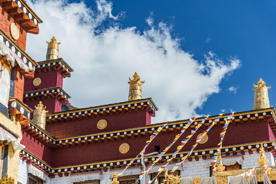 Maroon monastery building with gold finials and prayer flag corner