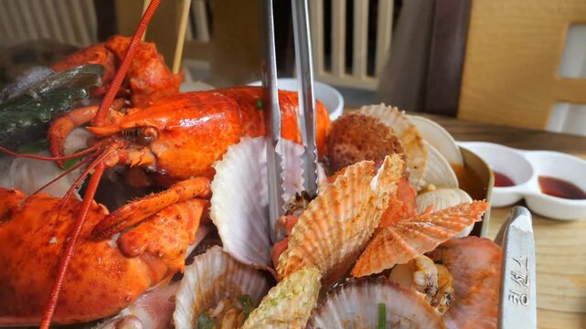 A large tray holds a variety of steam cooked seafood including a red lobster, scallops, clams, and octopus