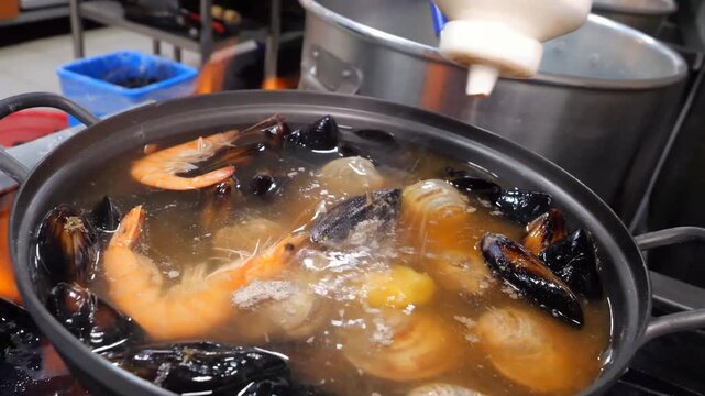 Delicious seafood soup preparation featuring assorted shellfish and fresh vegetables simmering over high heat in restaurant kitchen