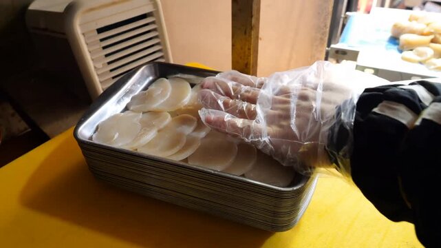 Freshly sliced scallop portions are carefully arranged on metallic trays and wrapped securely in plastic film within a commercial kitchen environment for distribution