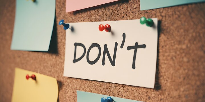 A significant reminder note with the word DONT firmly pinned on a textured cork board