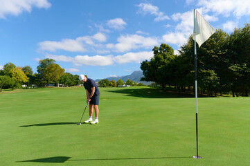 Obraz premium Man putting golf ball on green course.