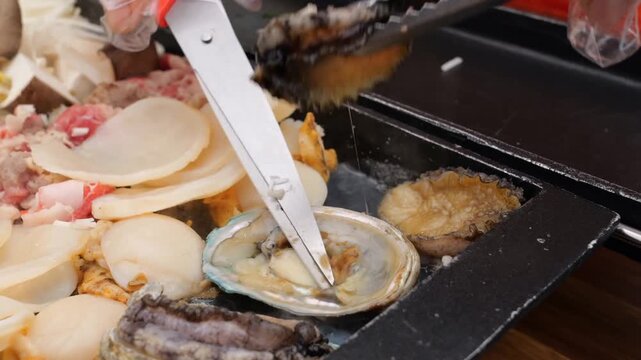 Various proteins including seafood and meats cook on a hot griddle alongside fresh vegetables and herbs, then get transferred into dipping sauces and plates for a meal service
