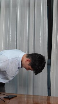 Asian young man standing up from a desk, and bowing deeply to apologize, corporate mistake and regret concept, vertical video