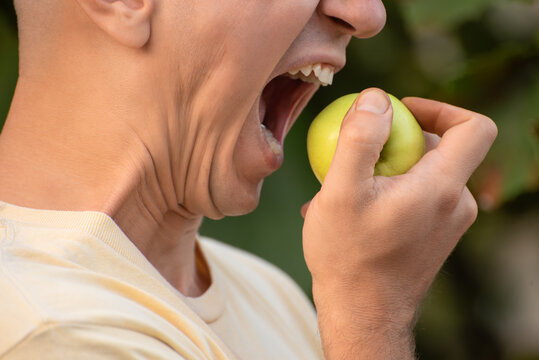 Young man bites into a vibrant green apple, mouth wide open in a fresh outdoor close up that highlights healthy eating, natural nutrition and wholesome snack enjoyment