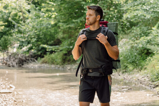 Male hiker with backpack standing in a forest stream during an outdoor trekking adventure