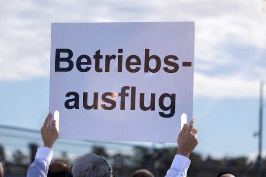 (Fotomontage) Ein Schild mit dem Text BETRIEBSAUSFLUG wird in die H&ouml;he gehalten