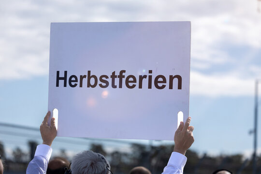 (Fotomontage) Ein Schild mit dem Text HERBSTFERIEN wird in die H&ouml;he gehalten