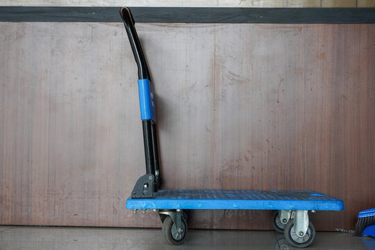 Blue industrial trolley with wheels and handle against a textured wall.